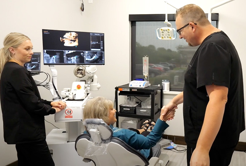 The image shows a group of people in a medical setting, including a dentist and patients, with various dental equipment visible.