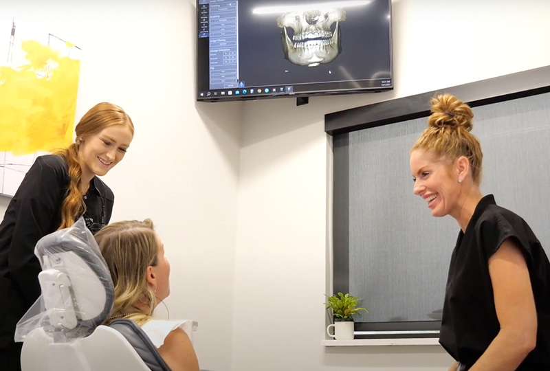 A group of people gathered around a dental chair with a 3D model of a skull on display, likely discussing medical or dental education or technology.