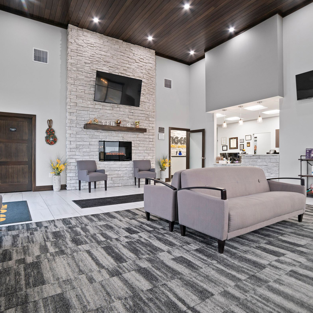 The image shows an interior view of a modern waiting area with a fireplace, seating, and a reception desk.