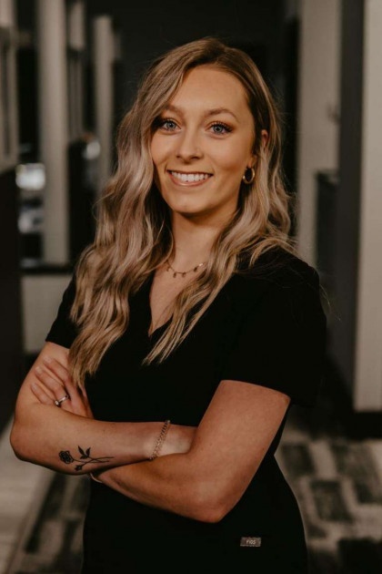 Woman with blonde hair wearing a black shirt and standing with arms crossed.